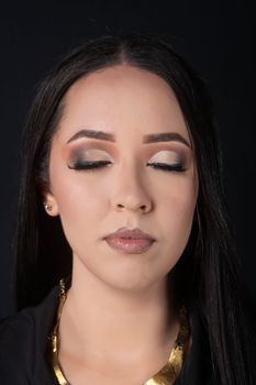 Brunette woman with glamorous makeup, eyes closed, showcasing sophisticated elegance in a studio portrait.