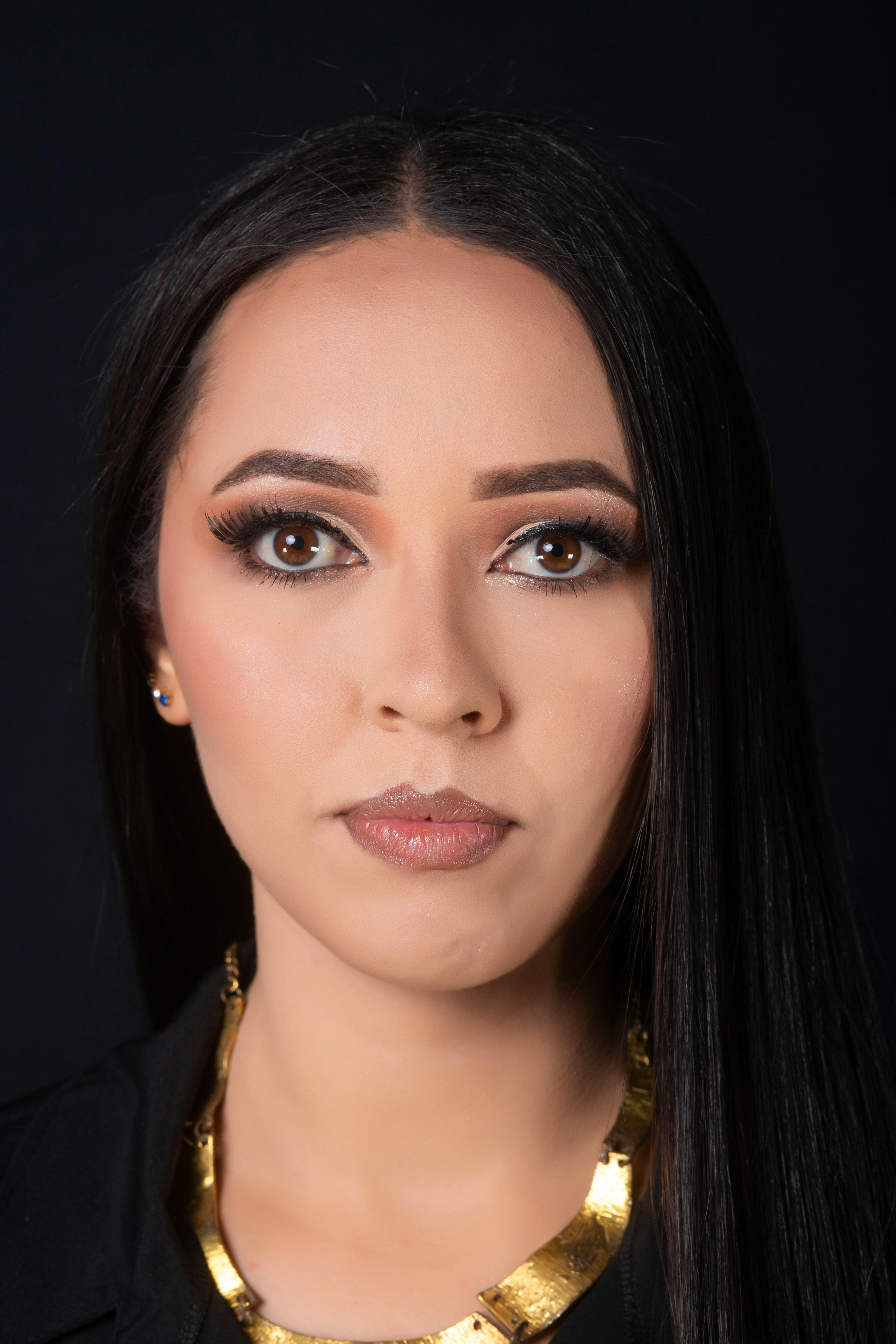 Close-up portrait of a brunette woman with bold makeup on a black background.