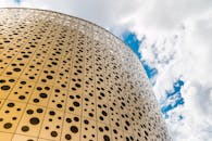 在明亮多云的天空下，低角度视角展现了现代摩天大楼的穿孔几何立面