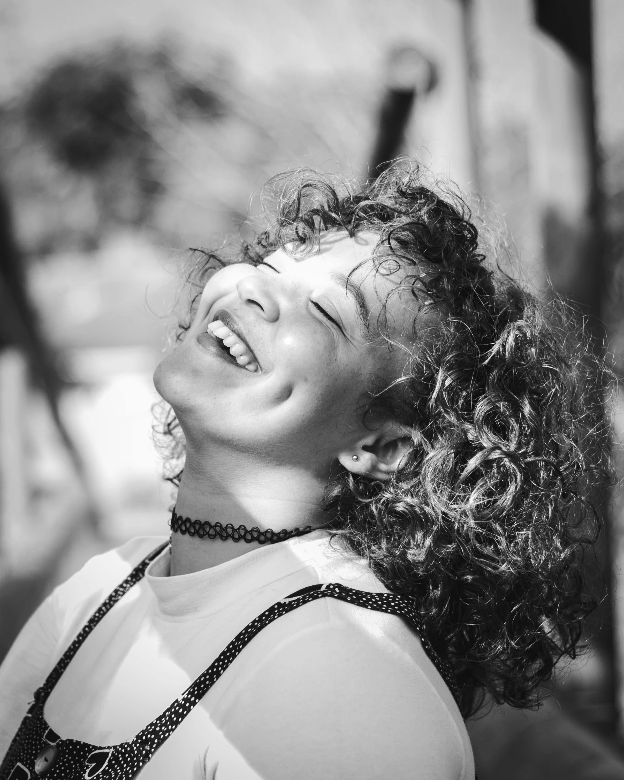 Black and white portrait of a woman laughing with eyes closed, showcasing carefree joy and curly hairstyle.