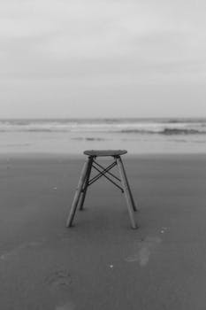 A black and white beach scene featuring a solitary chair on the sand, perfect for minimalist design.