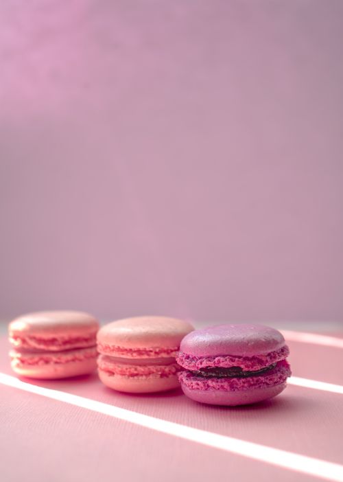 Free A close-up shot of pink and purple macarons aligned against a soft pastel background, showcasing delicate texture and color contrast. Stock Photo
