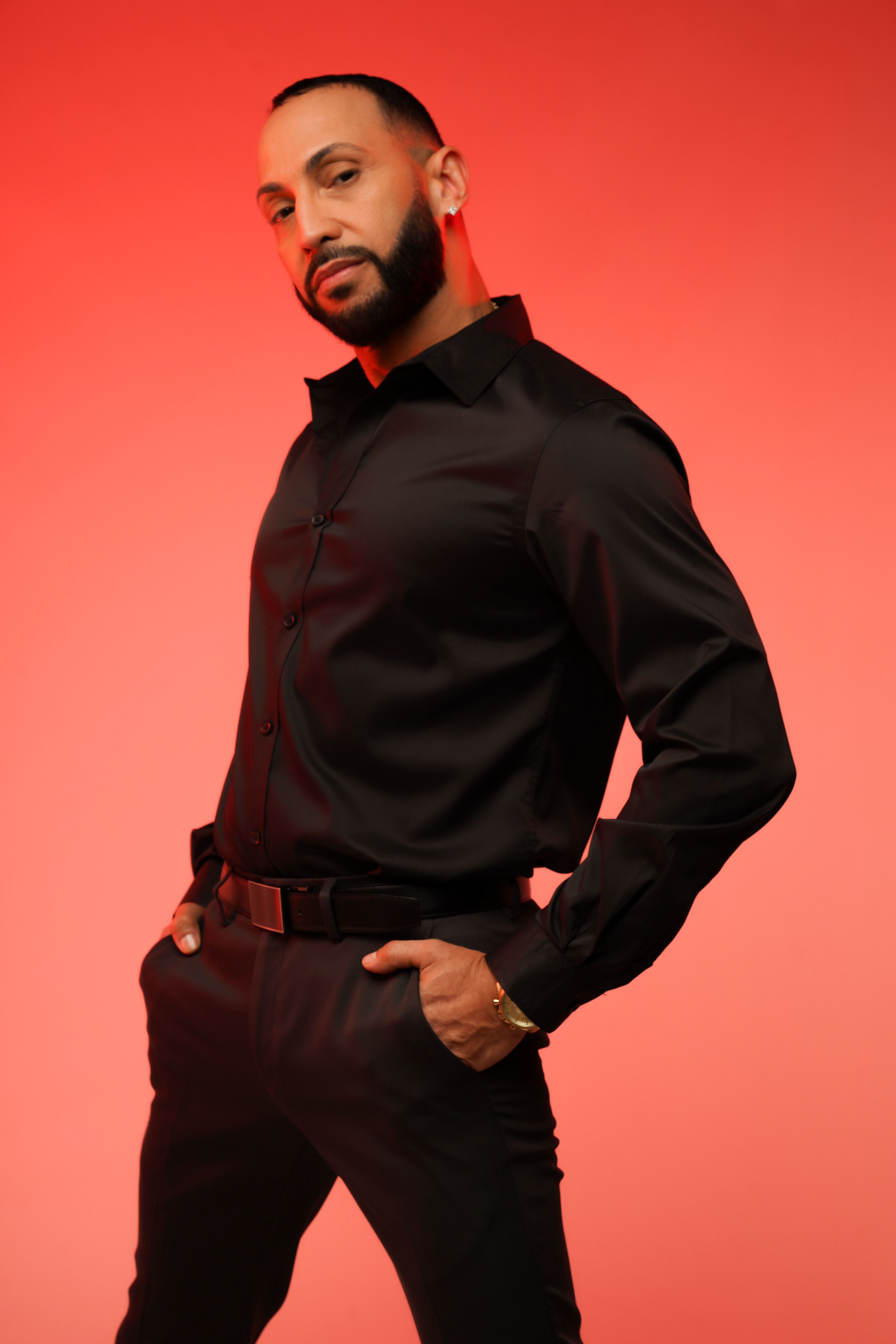 Fashion portrait of a bearded man in a black outfit against a red background.