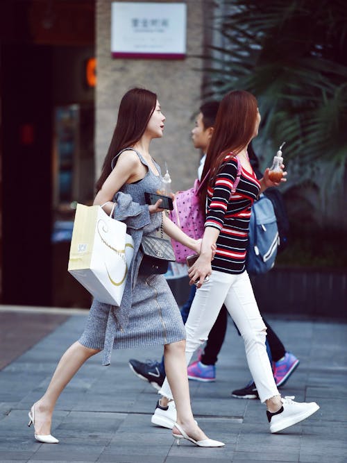 Two Women Holding Glass Bottles Standing Near Brown Wall