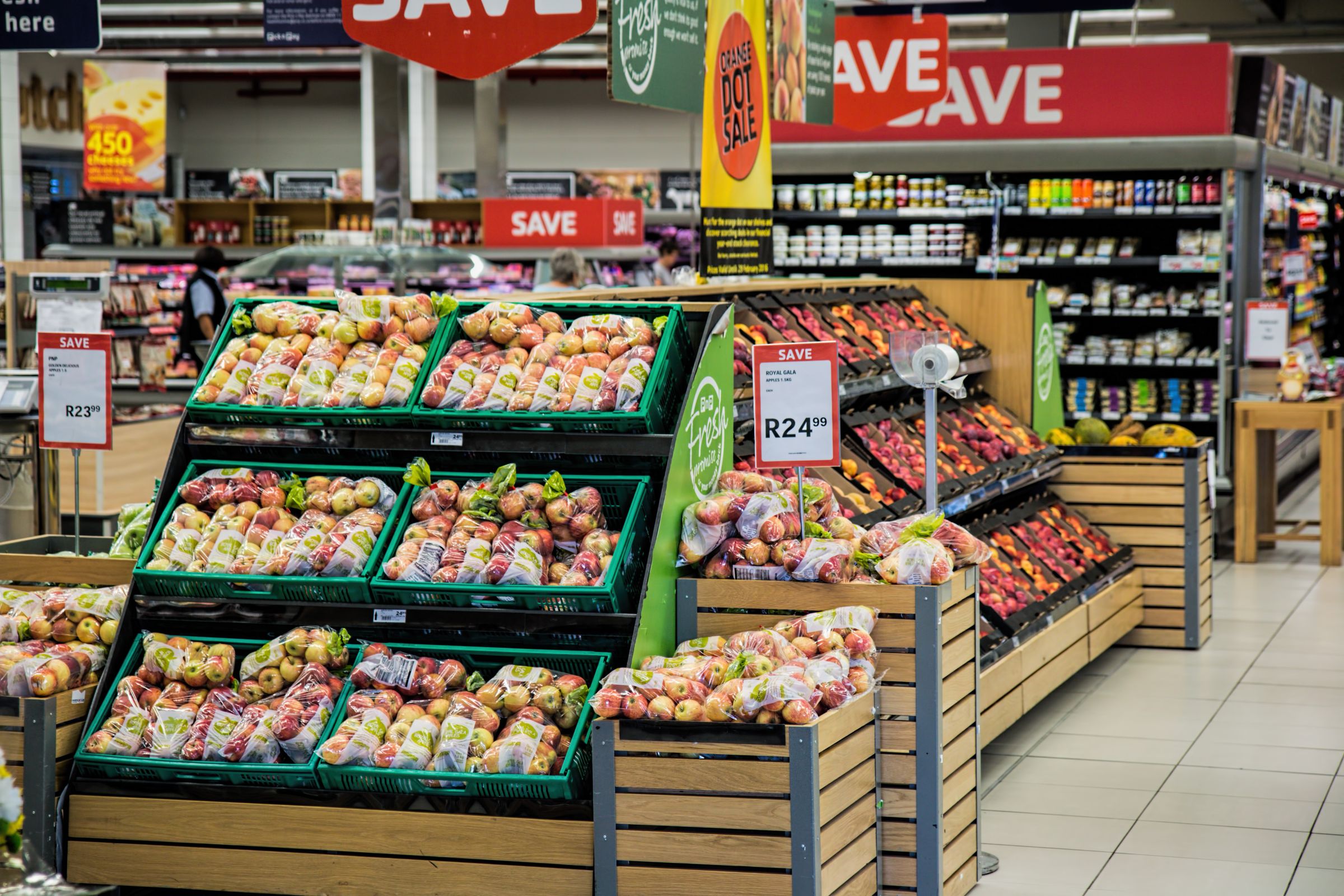 A supermarket aisle crowded with produce displays and red promotional price signs