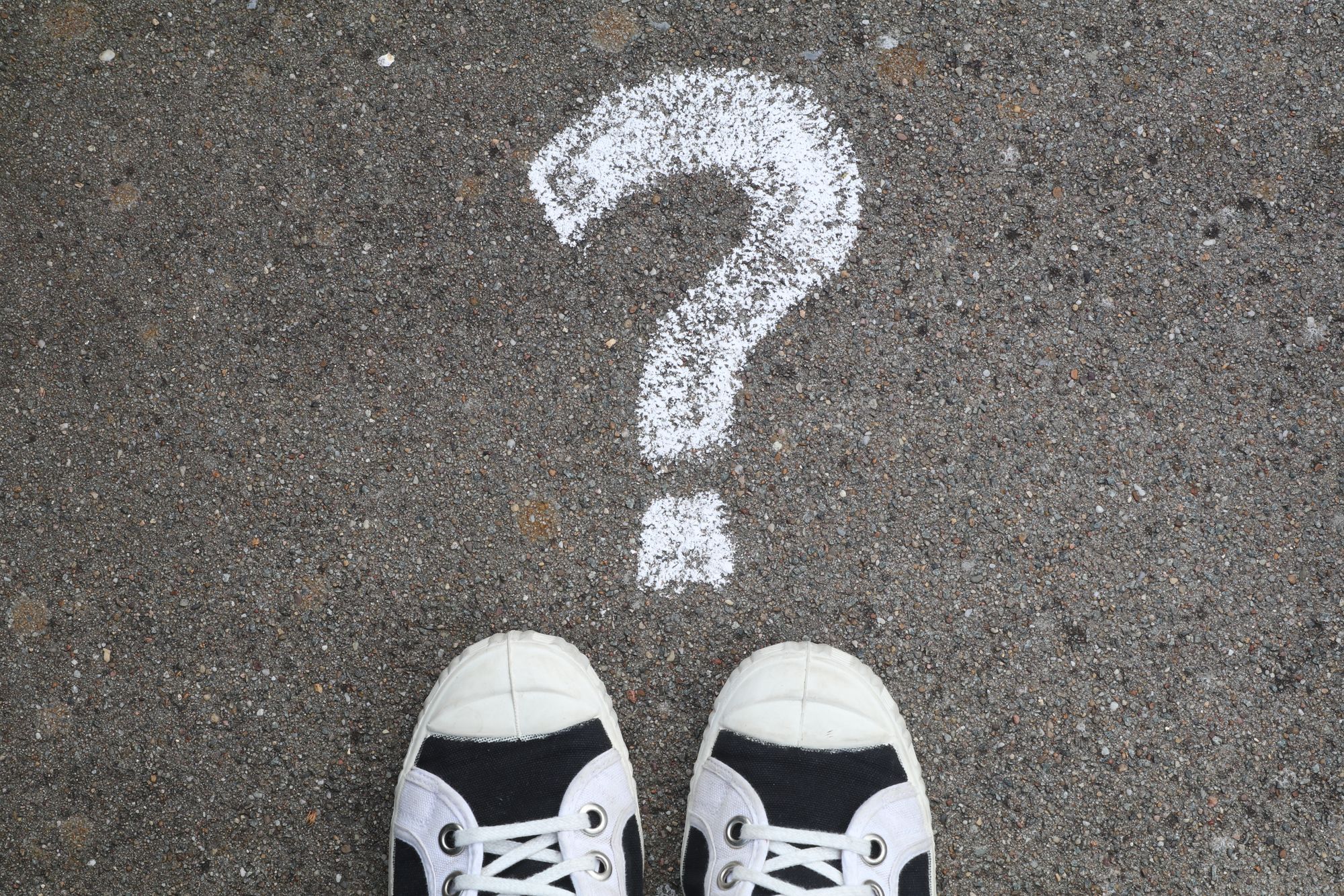 Sneaker vor einem mit Kreide gezeichneten Fragezeichen auf dem Boden