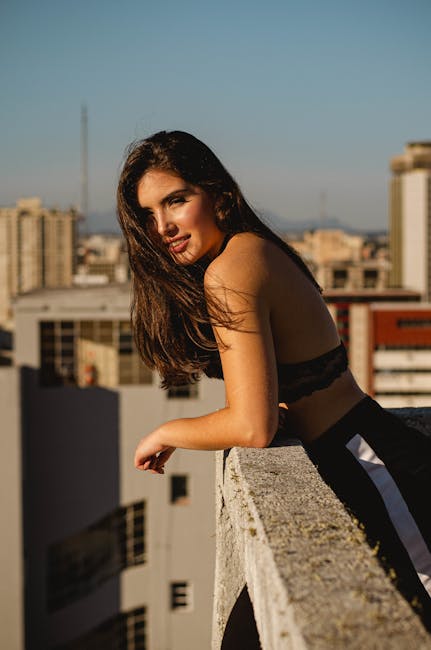 Portrait of a young woman leaning on a rooftop ledge with an urban cityscape backdrop.