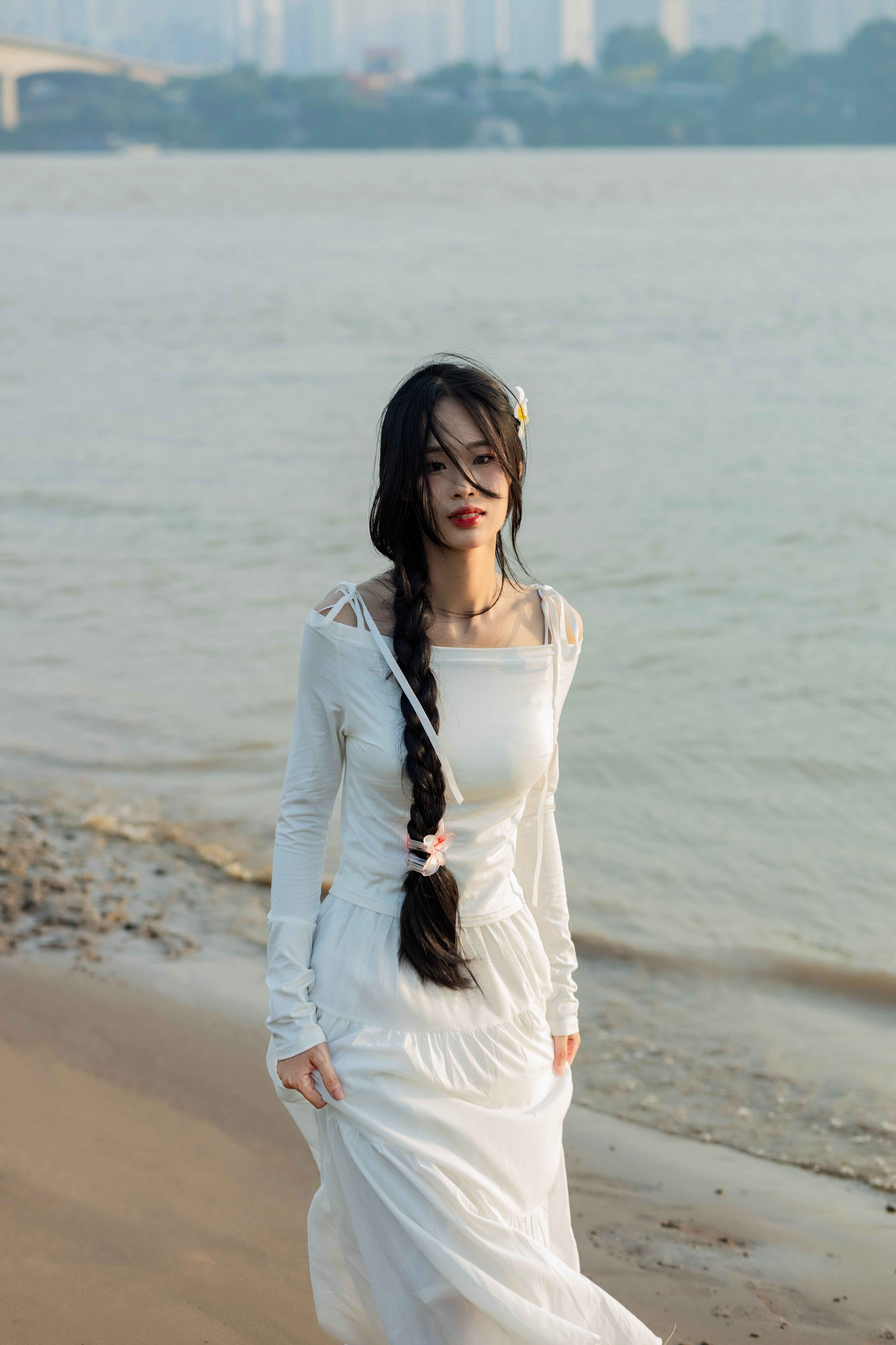 Serene scene of a woman with long braid in a white dress strolling on a beach.