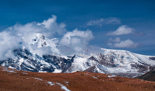 Free Stunning snowy mountains with clouds under a clear blue sky. Stock Photo