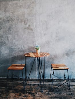 A minimalist wooden table with stools and a concrete wall background, ideal for modern interiors.