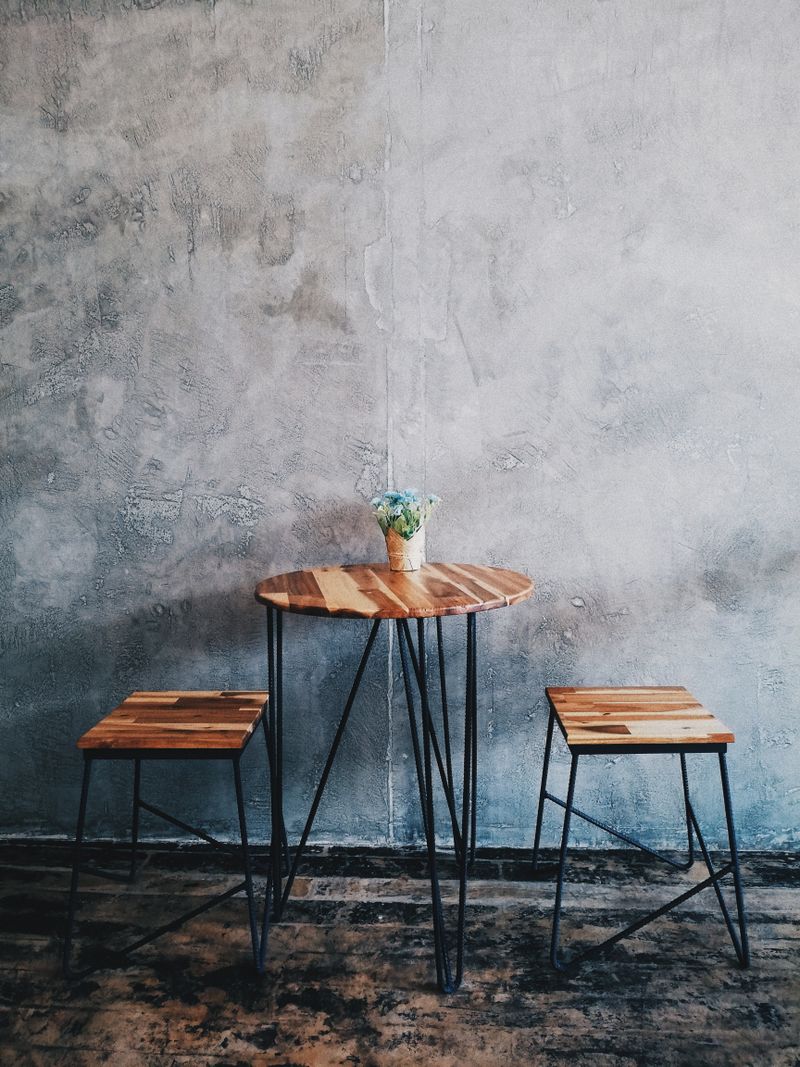A minimalist wooden table with stools and concrete wall background