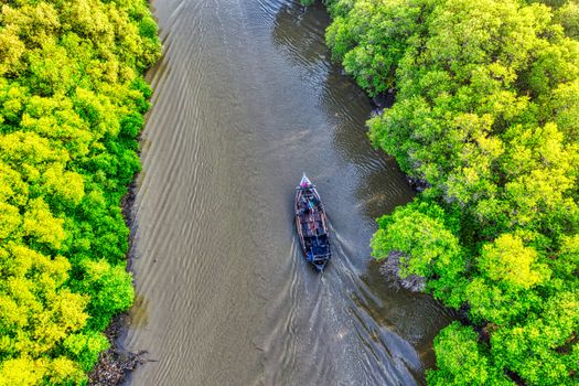 Drone shot of a boat navigating through lush green mangrove river in Banten, Indonesia.