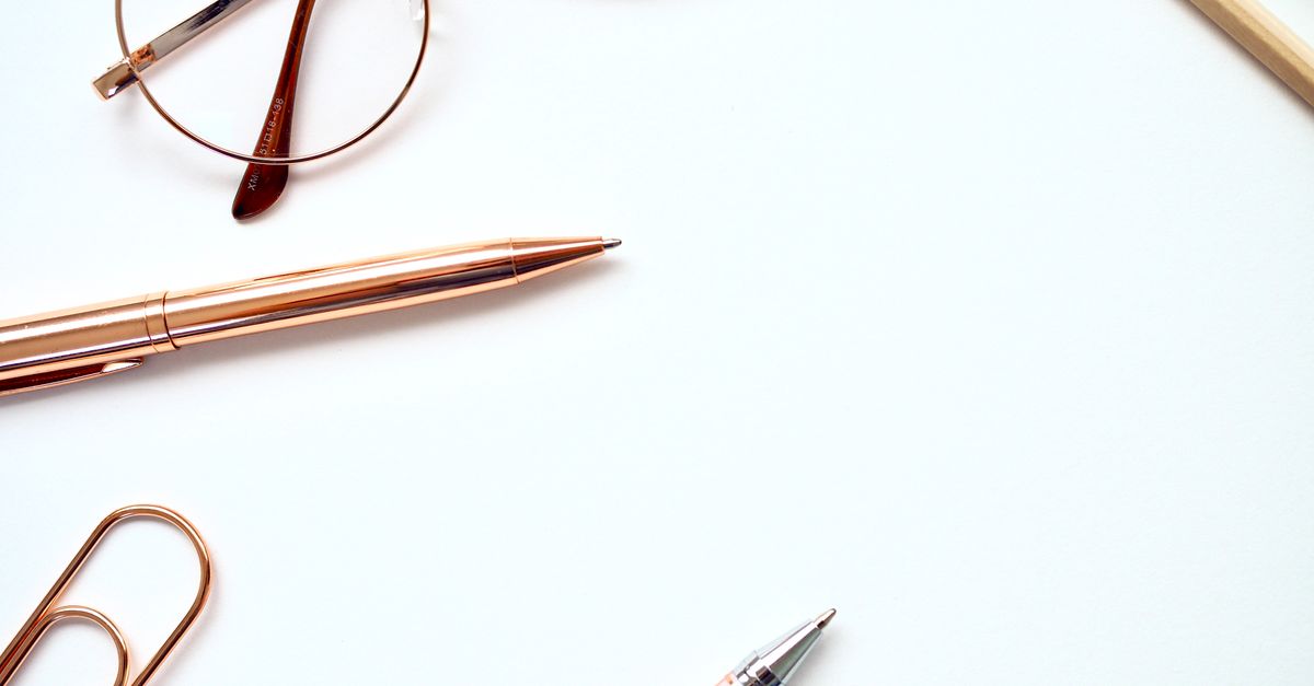 Top view of a stylish minimalist desk setup featuring pens, eyeglasses, and paperclips on a white background.