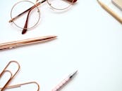 白色背景上，一支钢笔、一副眼镜和一枚回形针的特写，展现了一个时髦的极简主义书桌设置的顶视图