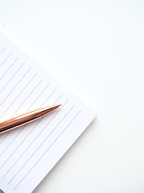 A close-up shot of a gold pen on a lined notepad with a white background, offering ample copyspace.