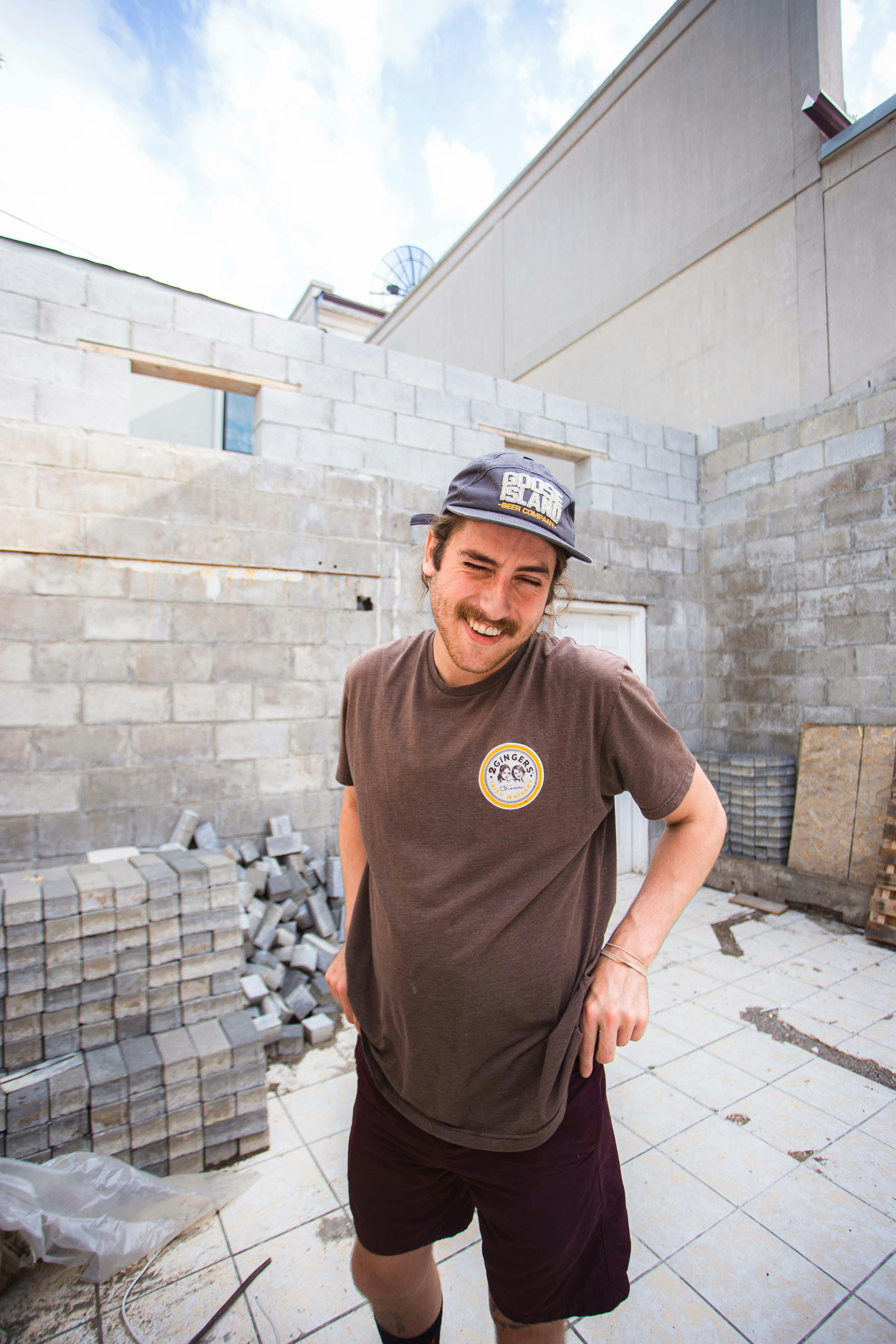 一名戴帽子的男子微笑着站在建筑区的砖块旁