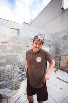 一名戴帽子的男子微笑着站在建筑区的砖块旁