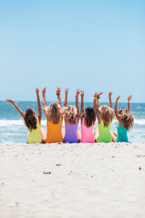 Free Back view photo of six girls wearing swimsuit sitting on white sand Stock Photo