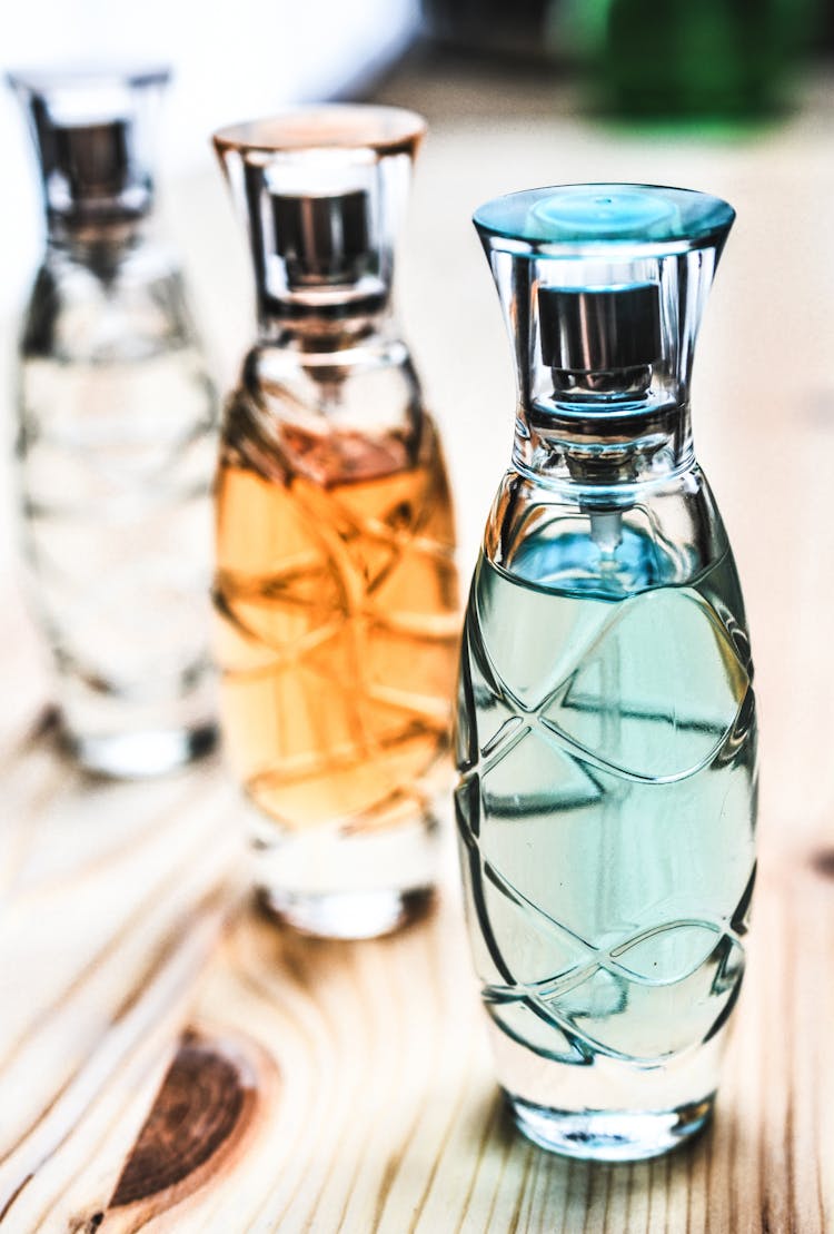 Three Assorted Clear Glass Perfume Spray Bottles On Brown Wooden Surface