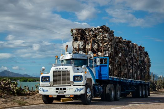A Mack truck loaded with scrap metal travels on a rural road under a cloudy sky.