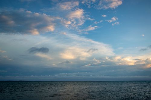Free A tranquil ocean scene under a dramatic cloudy sky at sunset. Stock Photo