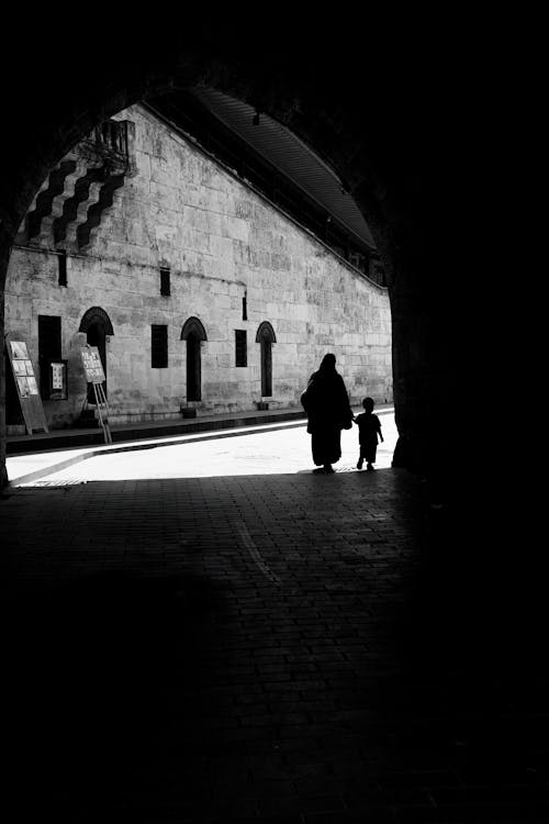 A black and white photo of two people walking through an archway