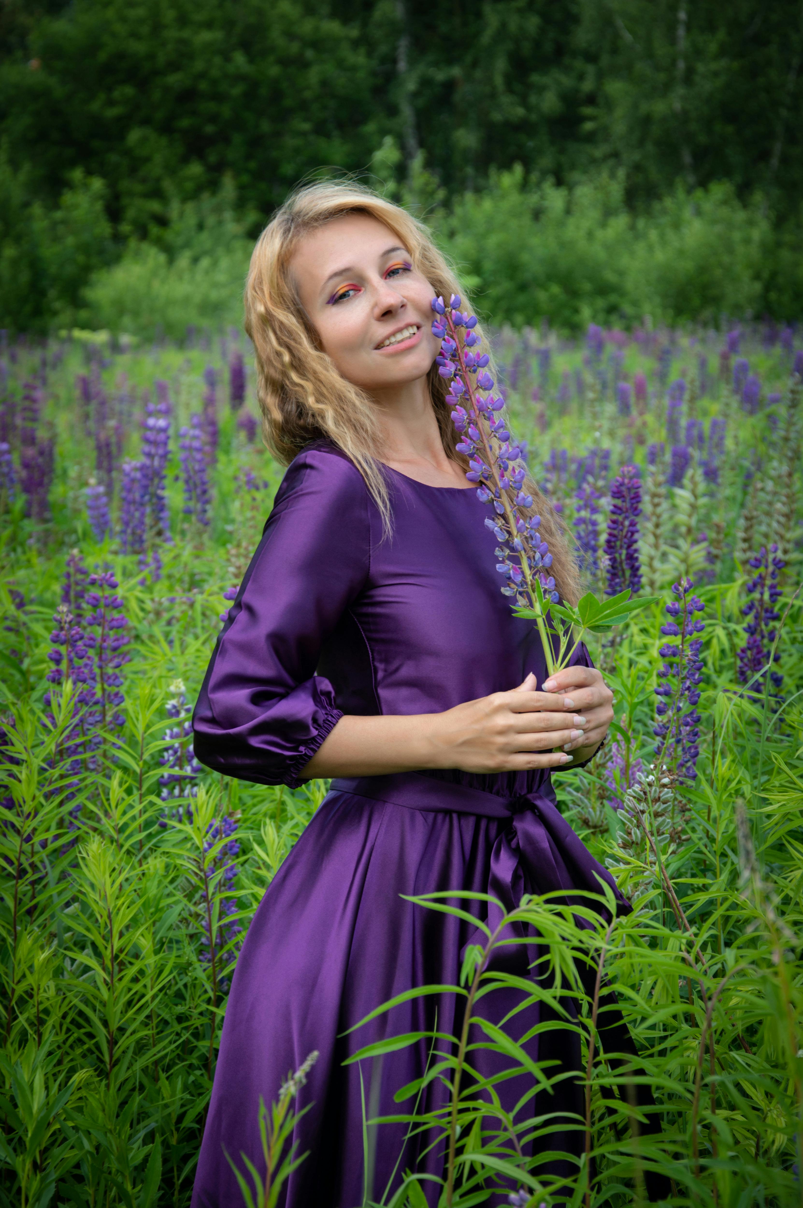A woman in a purple dress stands in a lavender field, embracing nature's beauty.