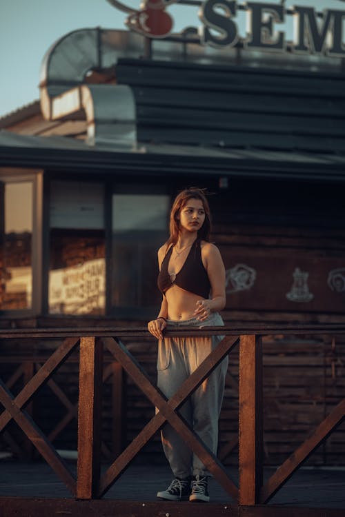 A woman in a sports bra and pants standing on a wooden fence