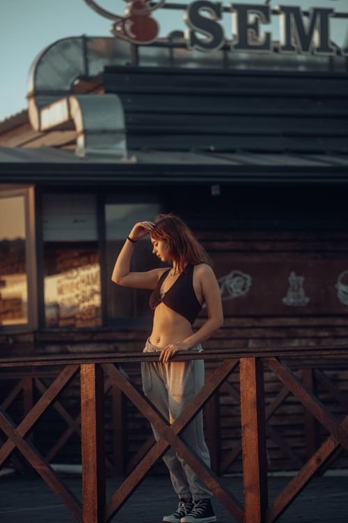 Free Stylish woman in a bikini top posing on a wooden fence during golden hour in an urban setting. Stock Photo