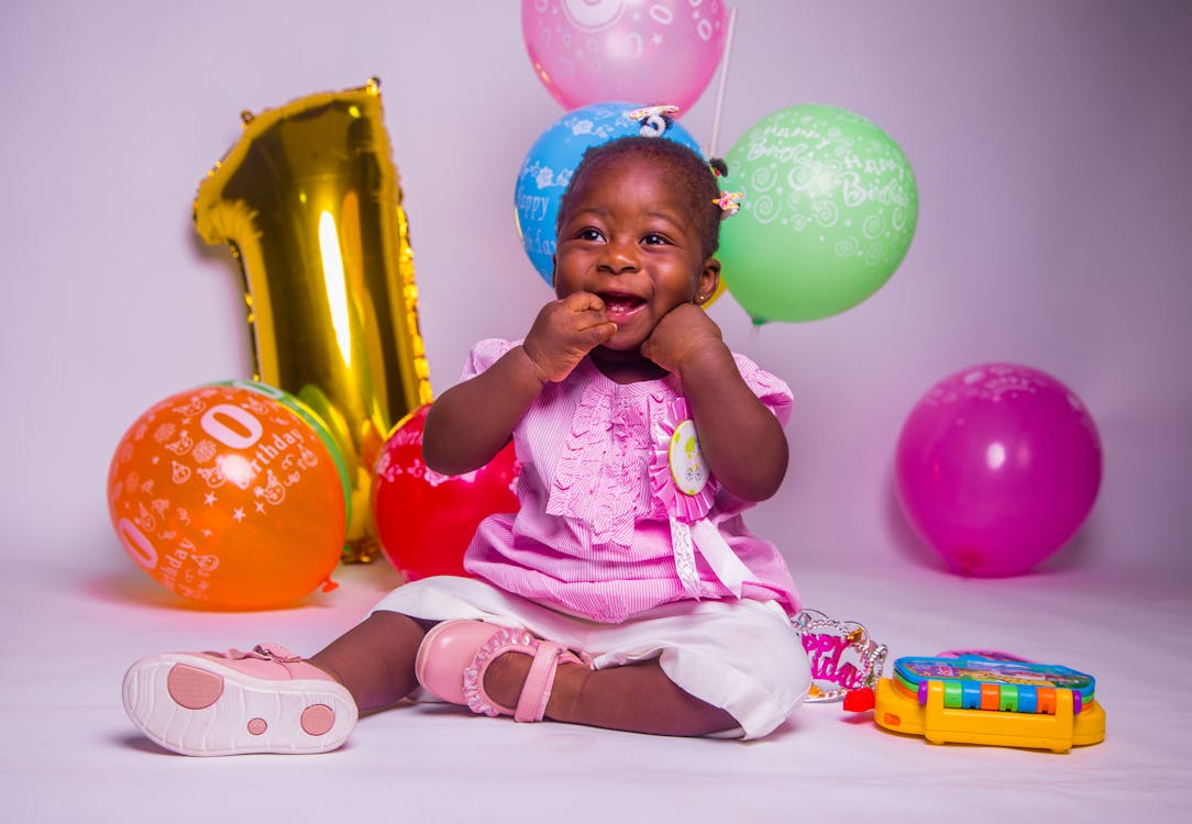 Linda niña de 1-2 años sentada en el suelo con globos de color rosa en