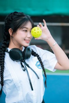 Portrait of a happy woman with long braids and headphones holding a yellow ball outdoors.