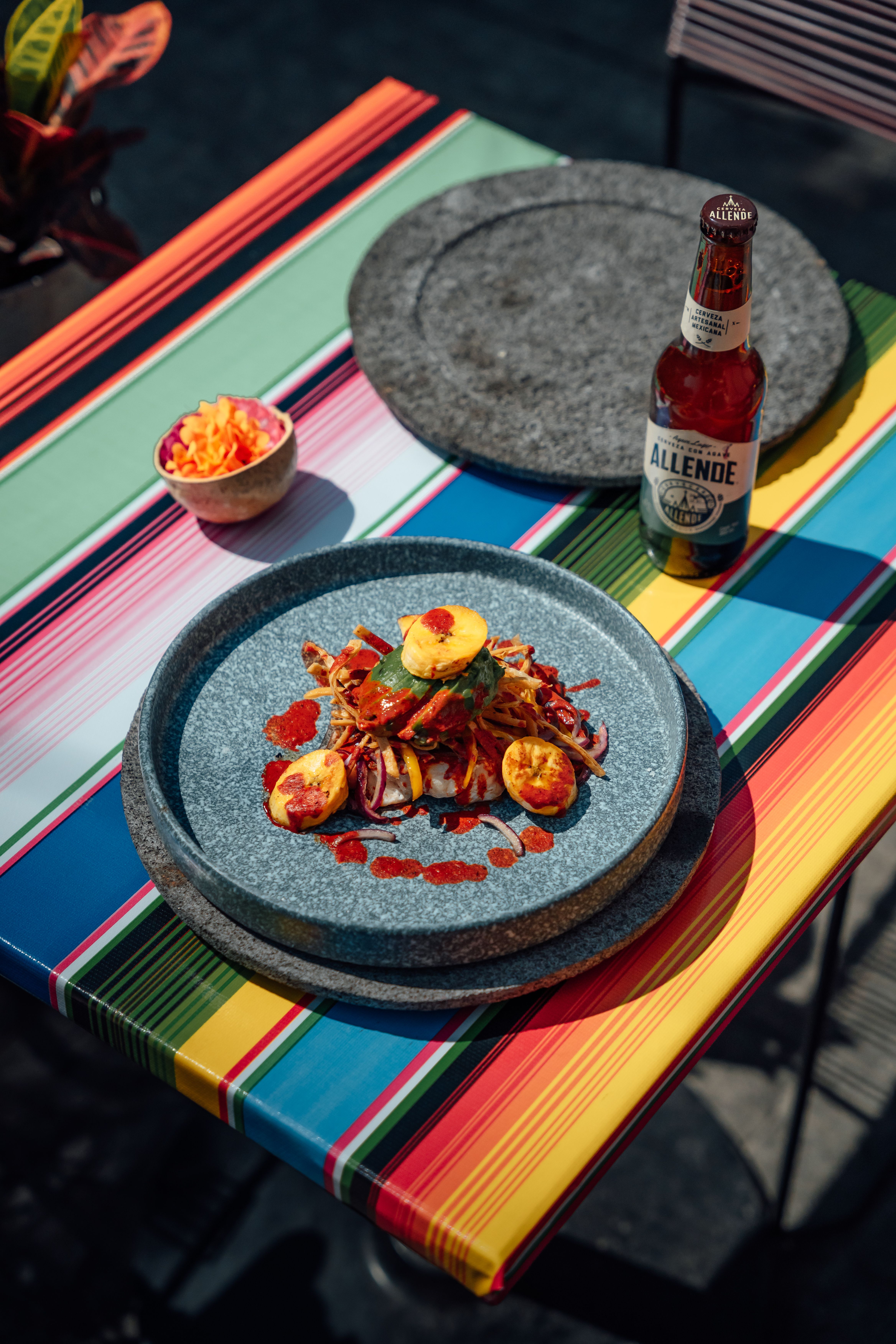 Vibrant pasta dish with beer on a colorful table in outdoor setting.