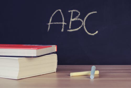 Two Books Beside Two Chalks. In the Backround, a blackboard with the letters ABC written on it in white.