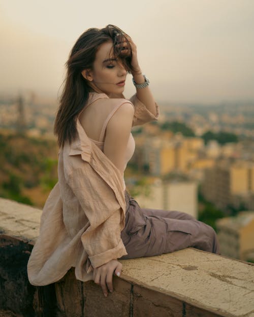 A woman sitting on a ledge with a city in the background