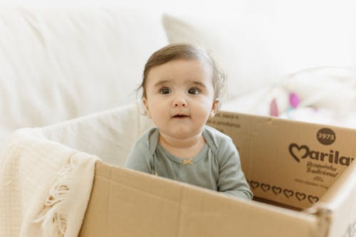 A baby sitting in a cardboard box with a white background