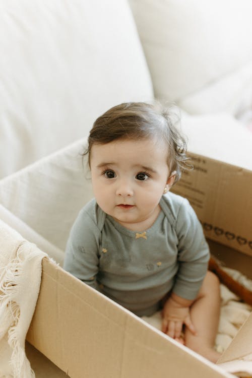 A baby sitting in a cardboard box with a toy