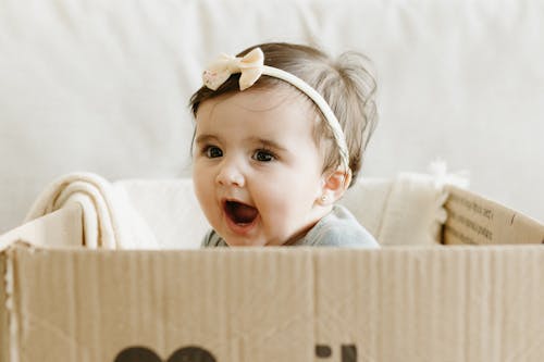 Free A baby is sitting in a cardboard box with a bow on it Stock Photo