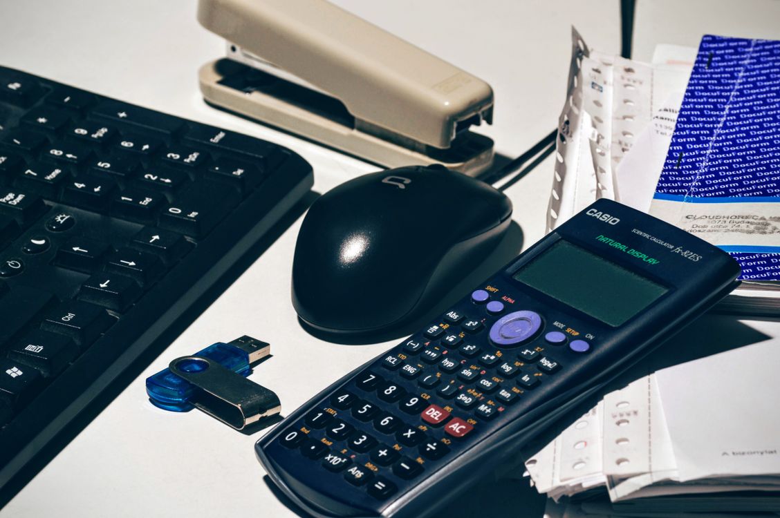 A desk set up for bookkeeping with a calculator, keyboard, and paperwork.