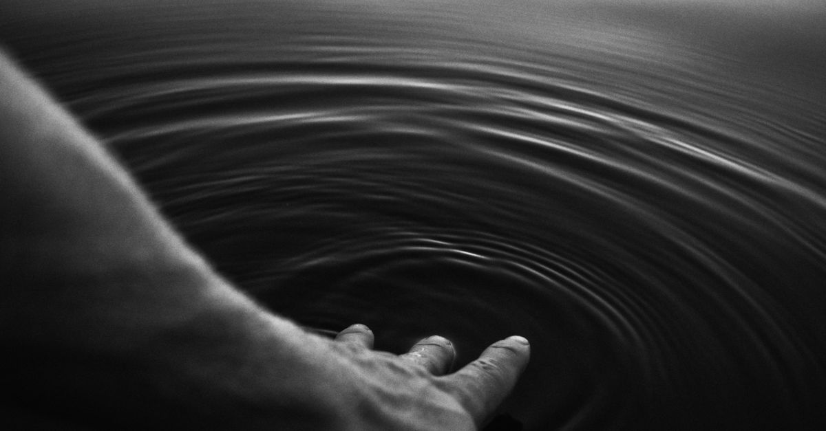 Imagem em preto e branco de uma mão criando ondas na água, evocando tranquilidade.