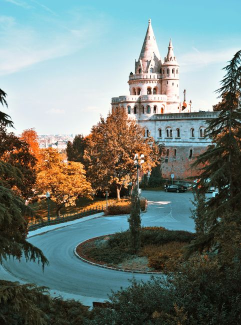 Picturesque castle surrounded by colorful autumn trees and winding road, ideal for travel enthusiasts.