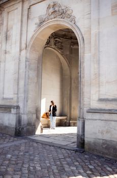 A woman stands under a historic stone archway in Copenhagen, Denmark, on a sunny day.
