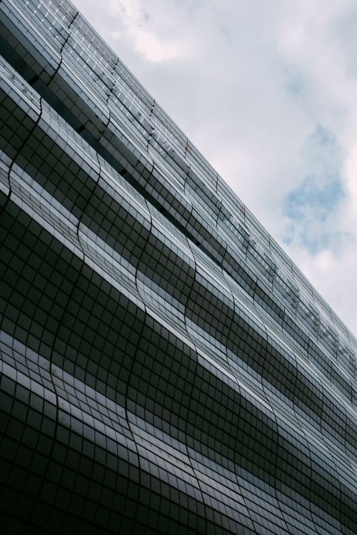 Free Vertical shot of a modern skyscraper with a futuristic facade against a cloudy sky, showcasing architectural design. Stock Photo