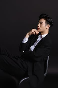 Young man in a black suit contemplating on a chair in studio. Fashion photography with a minimalist style.