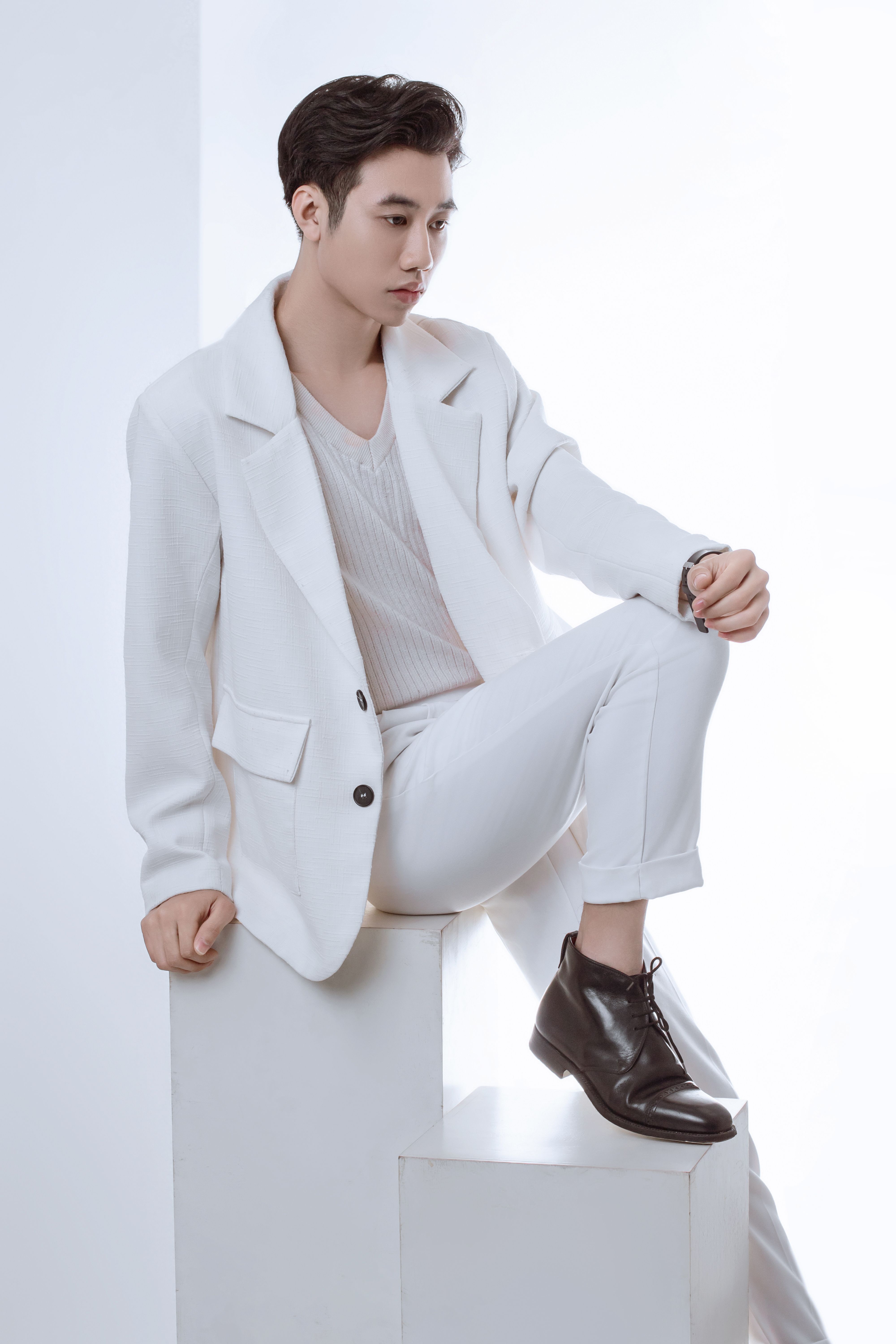 Sophisticated male model in a white suit posing stylishly in a studio setting.