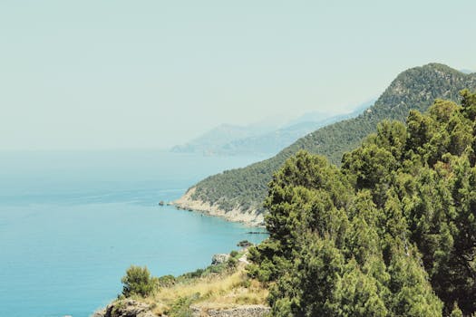 Stunning view of a tropical coastline with lush green mountains and clear blue sea, perfect for vacation and nature lovers.