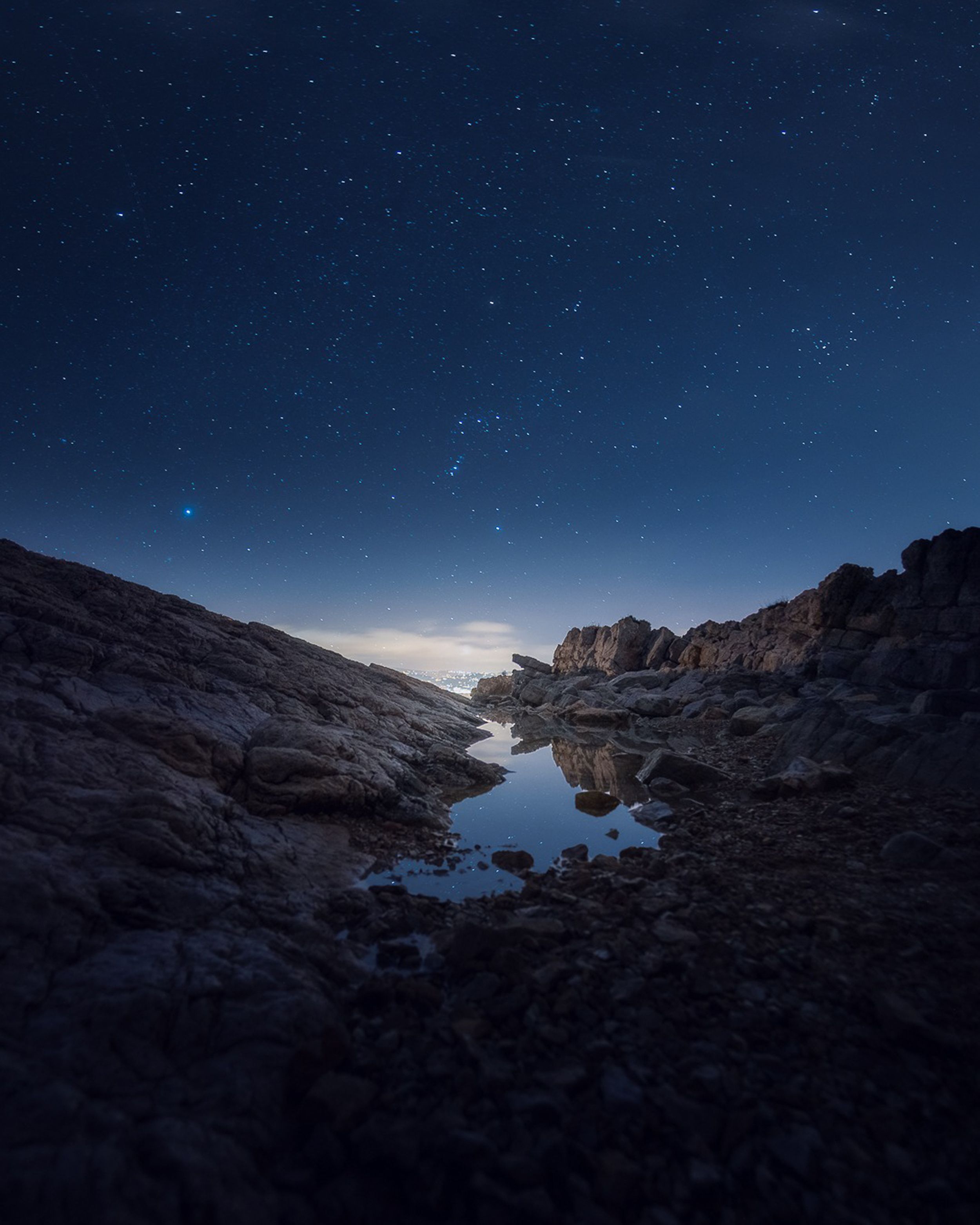 Capture of a tranquil rocky landscape beneath a vivid star-filled night sky.