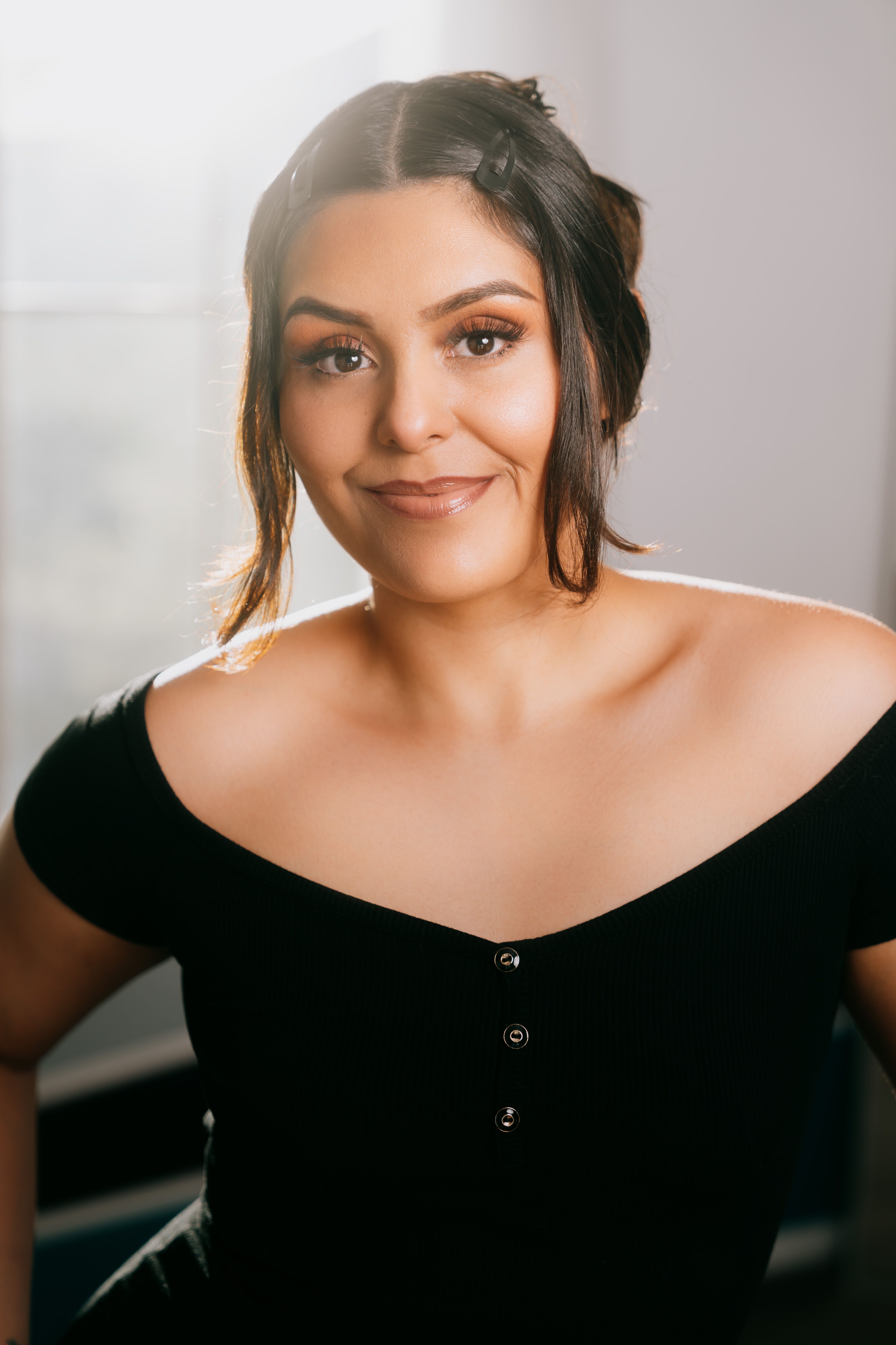 Elegantly posed woman in black dress, with soft lighting, smiling warmly.