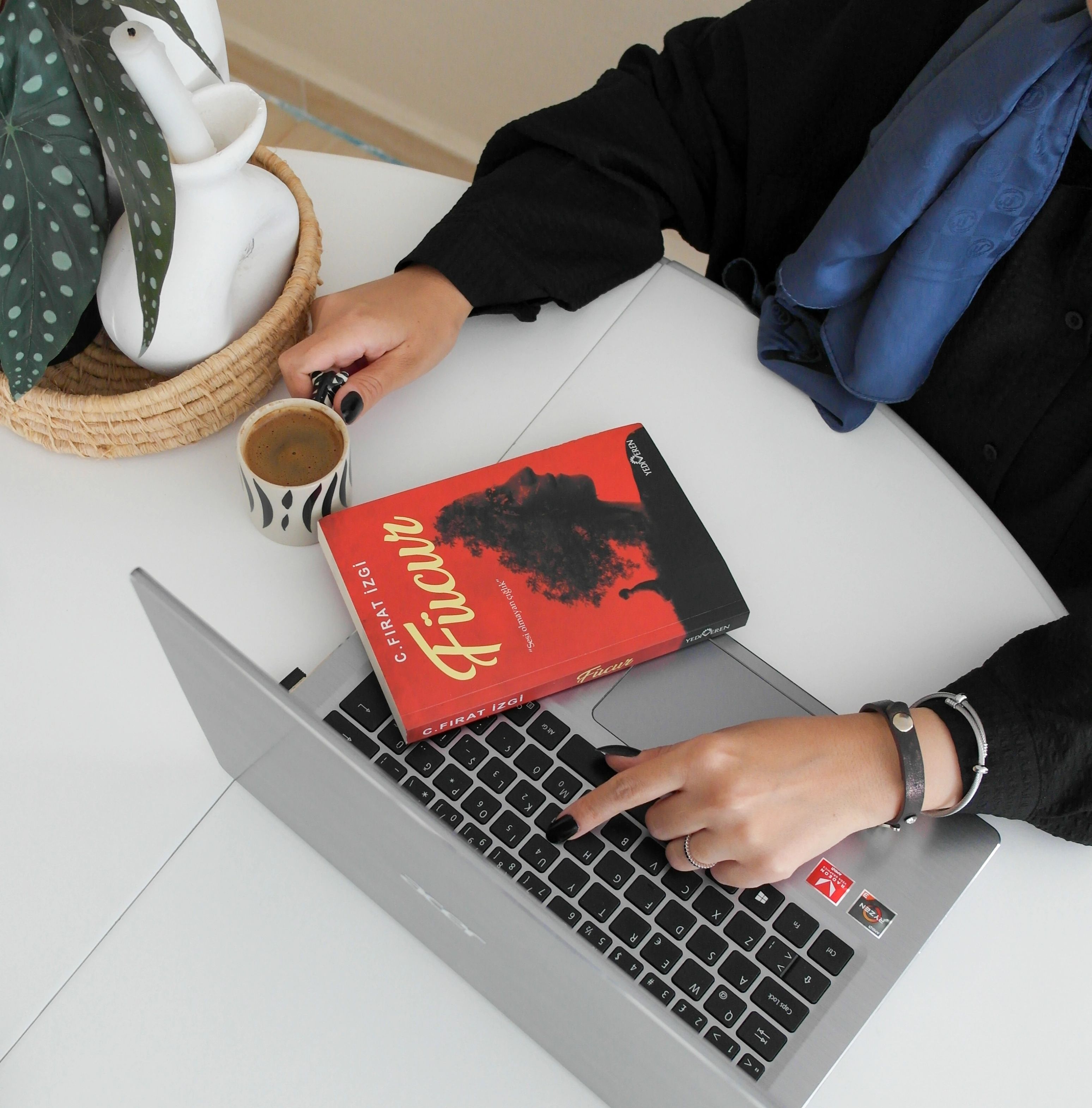 Overhead view of a woman working on a laptop with a coffee and a book.