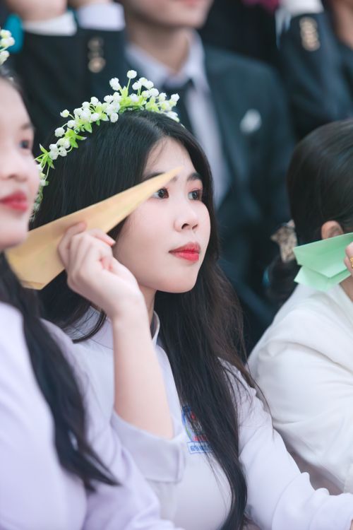 Free Captivating portrait of a young woman in a white shirt with floral wreath, focused on a paper plane indoors. Stock Photo
