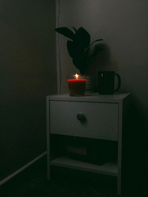 Free A warmly lit nightstand scene with a glowing candle, cup, and indoor plant creating a relaxing ambiance. Stock Photo